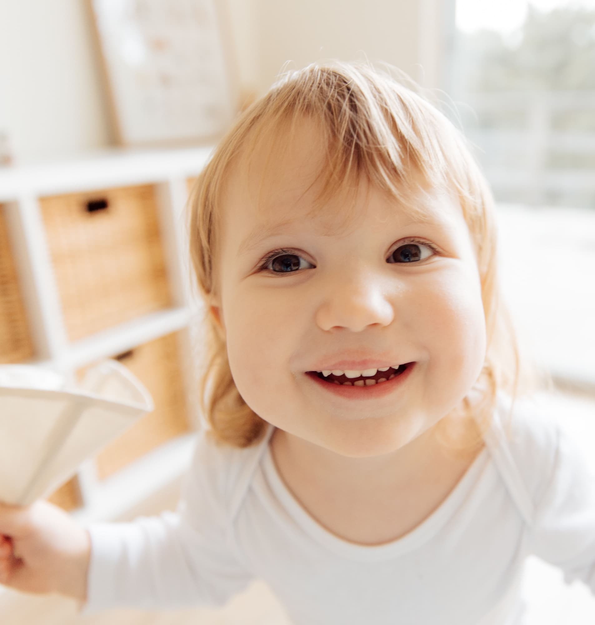 A smiling young child holding a paper airplane in a bright play space
